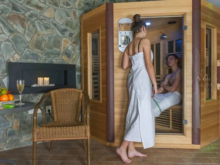 A sauna with a stone wall backdrop, a wicker chair, and a fruit platter.