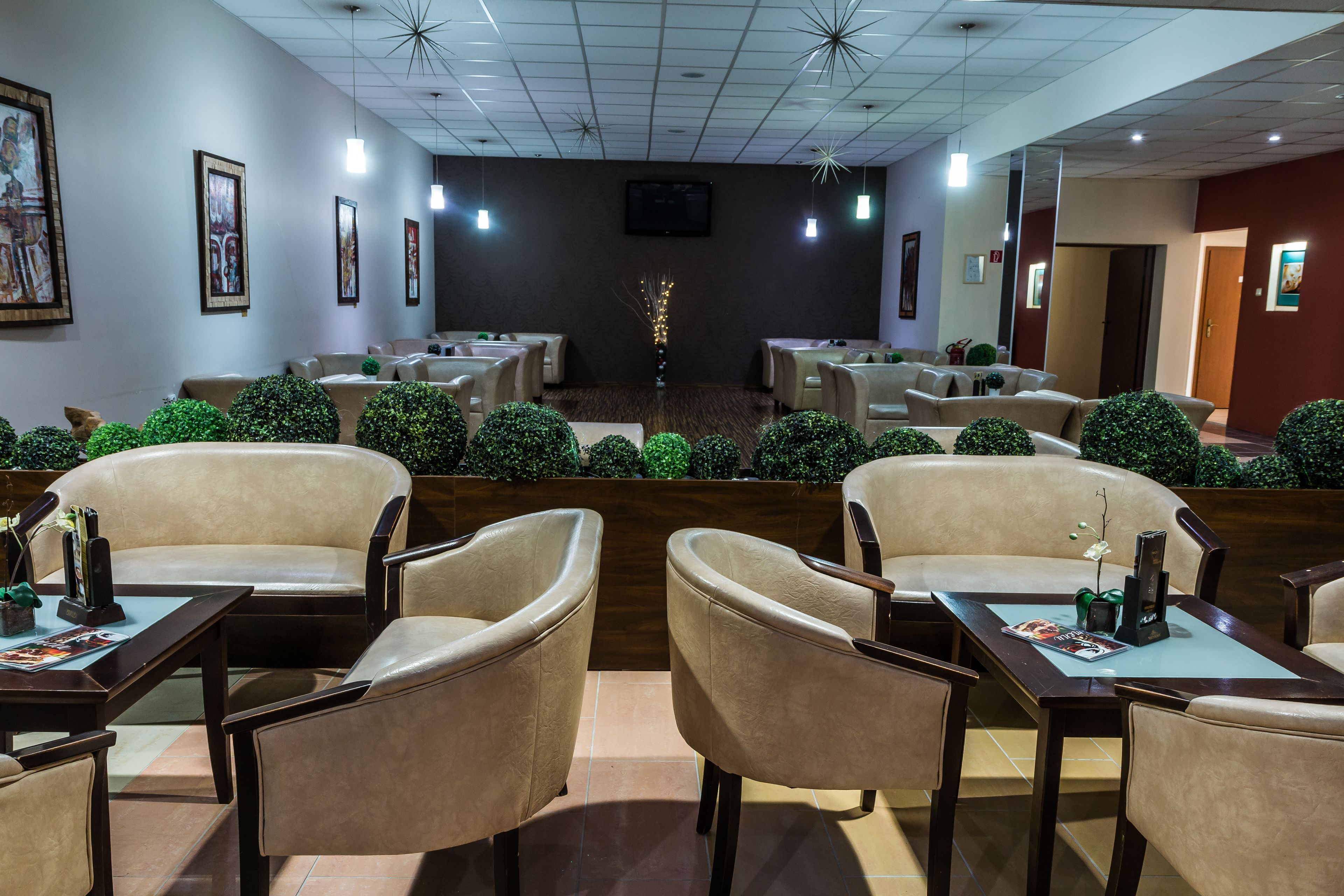 Un restaurante con varias mesas y sillas, un televisor montado en la pared y plantas decorativas.