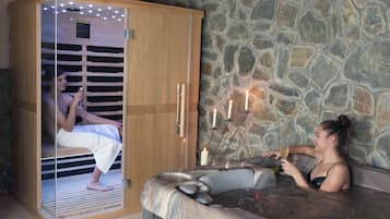 Et spa-rum med en stenvæg, et træskab med glasdør og et boblebad med stearinlys.