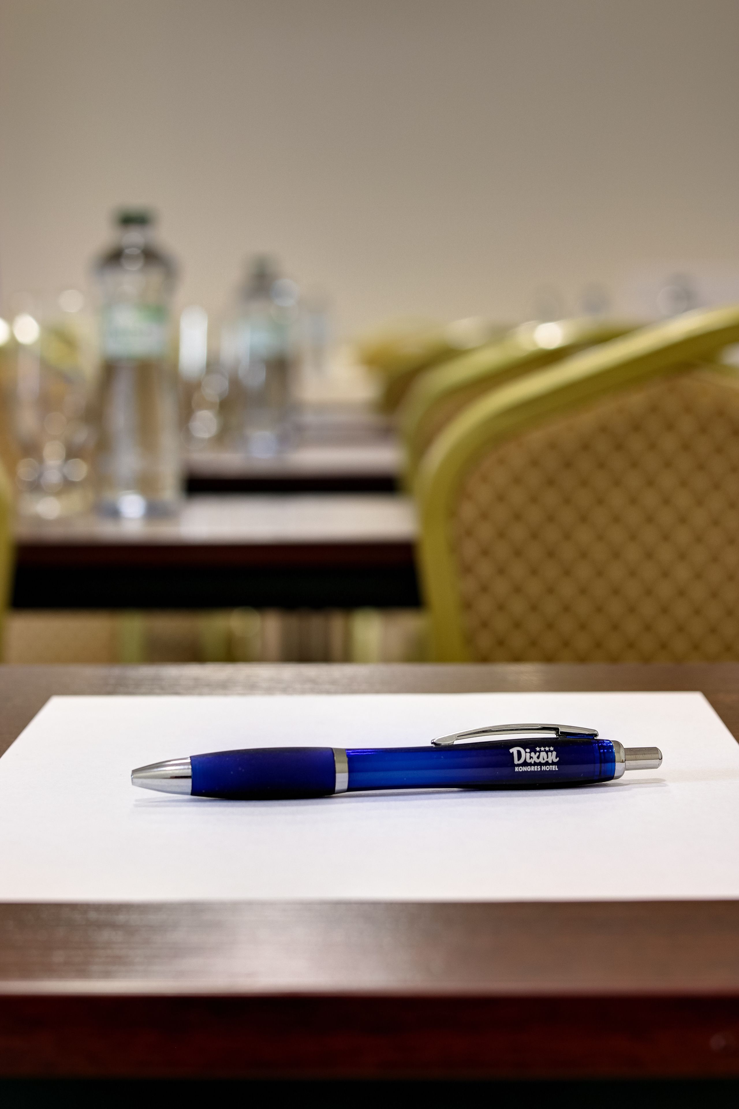 A pen on a white paper on a wooden table with a blurred background of a dining area.