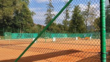 A tennis court with a chain-link fence, green netting, and a tennis ball machine.