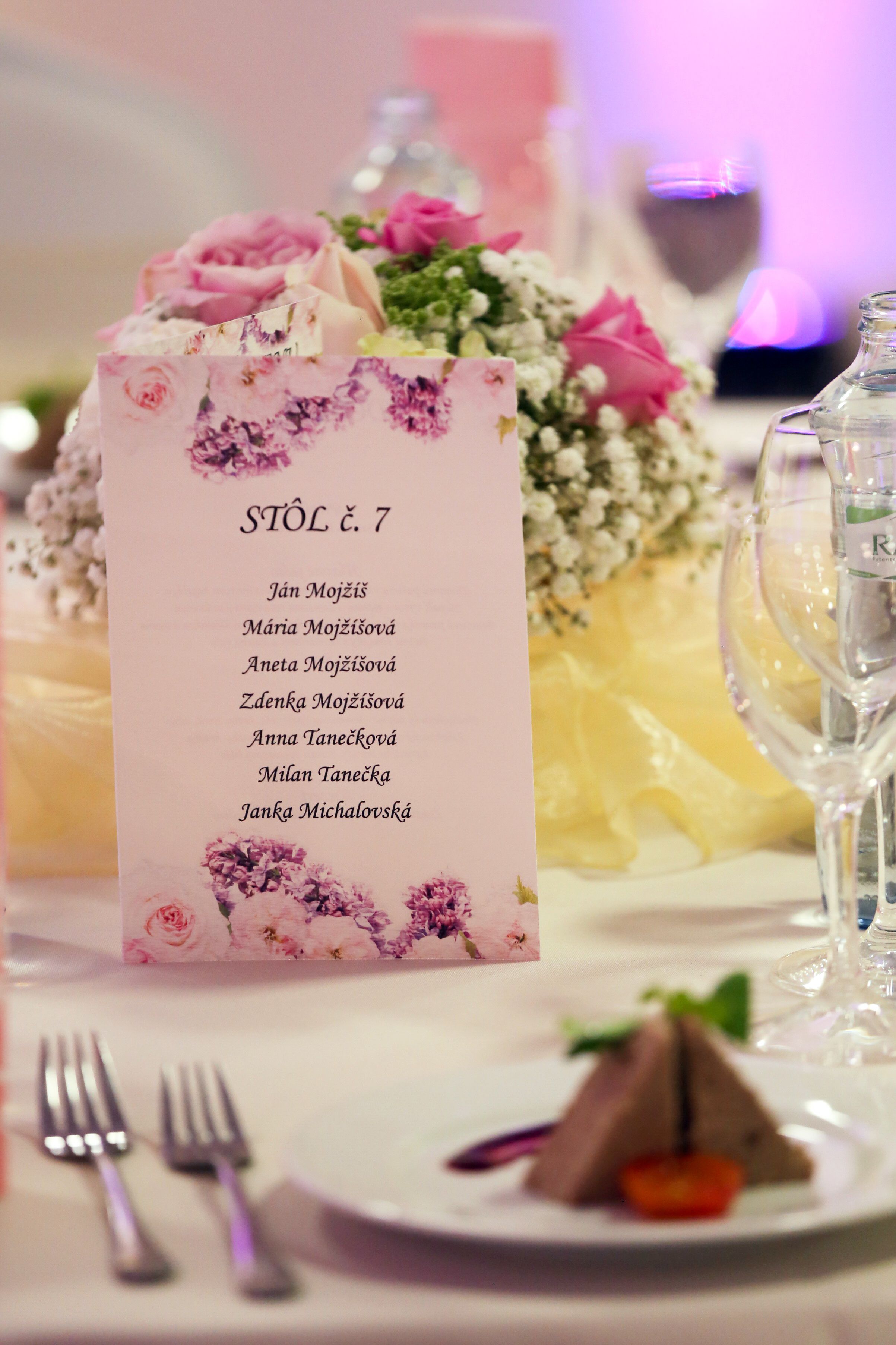 A table setting with a floral centerpiece, a menu card, and a glass of water.