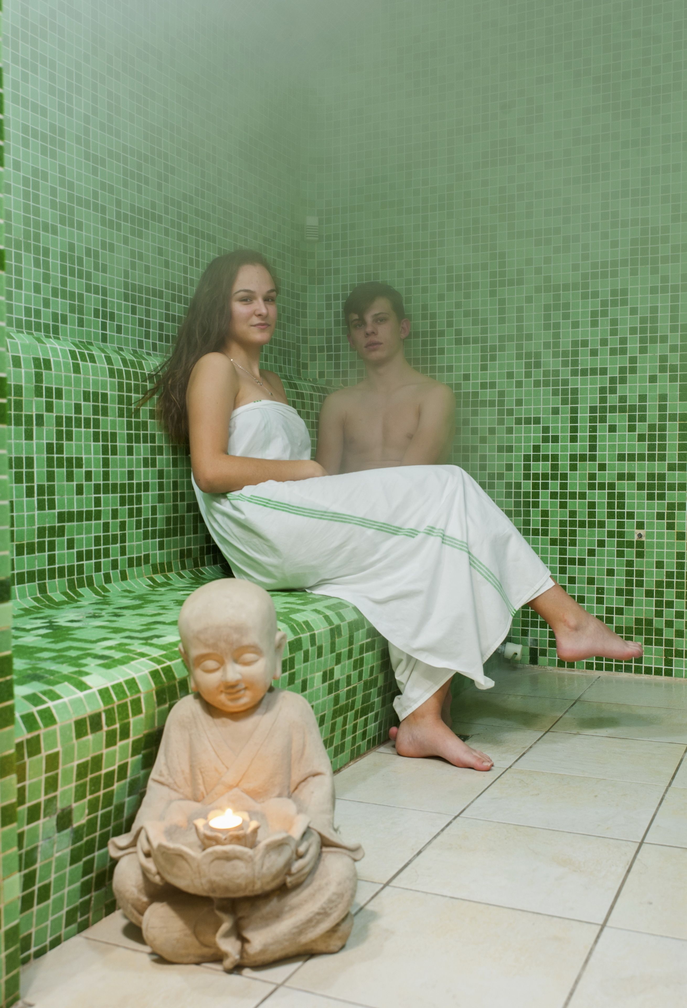 Et rum med en væg med grønne fliser, en hvid sofa og en statue af en figurerende person i meditation med et lys.
