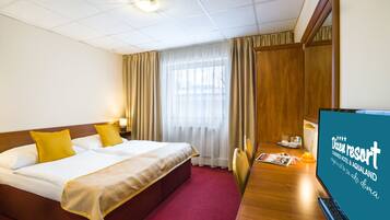 Una camera d'albergo con un letto, una scrivania con un computer e un televisore che mostra il nome dell'hotel.