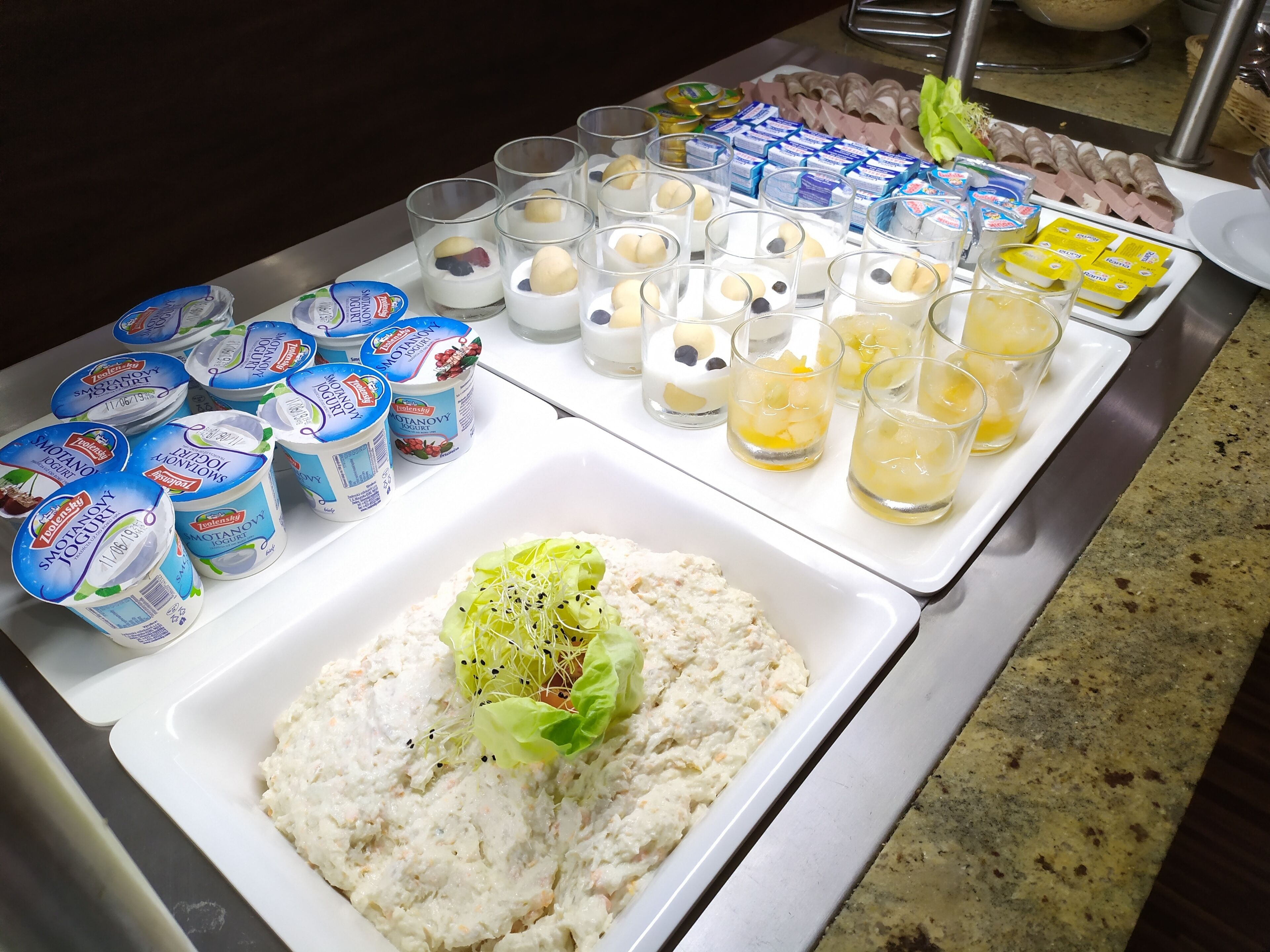 A buffet table with various food items including yogurt, fruit, and a salad.