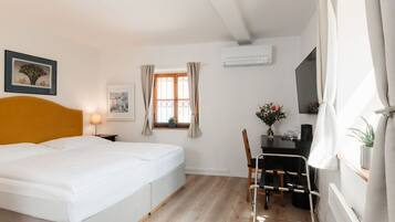A hotel room with a bed, a desk, a chair, a window with curtains, and a wall-mounted air conditioner.