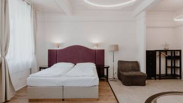 A modern hotel room with a double bed, two bedside tables, a chair, a small side table, and a wardrobe.