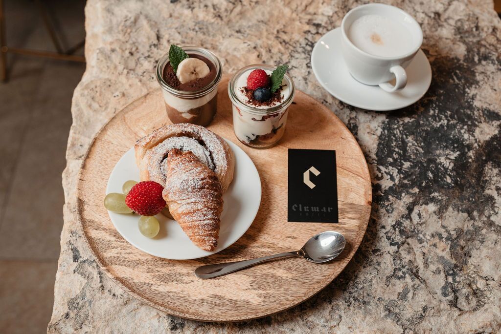 A dessert tray with a croissant, two dessert glasses, and a cup of coffee on a wooden board.