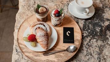 A dessert tray with a croissant, two dessert glasses, and a cup of coffee on a wooden board.