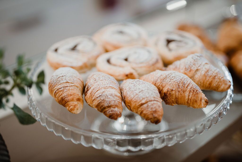 Un plateau en verre servant de présentoir, sur lequel on peut voir plusieurs pâtisseries, notamment des croissants et une viennoiserie enroulée, posé sur une table.