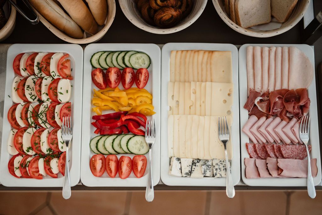 Three trays of food with various cheeses, cured meats, and vegetables.