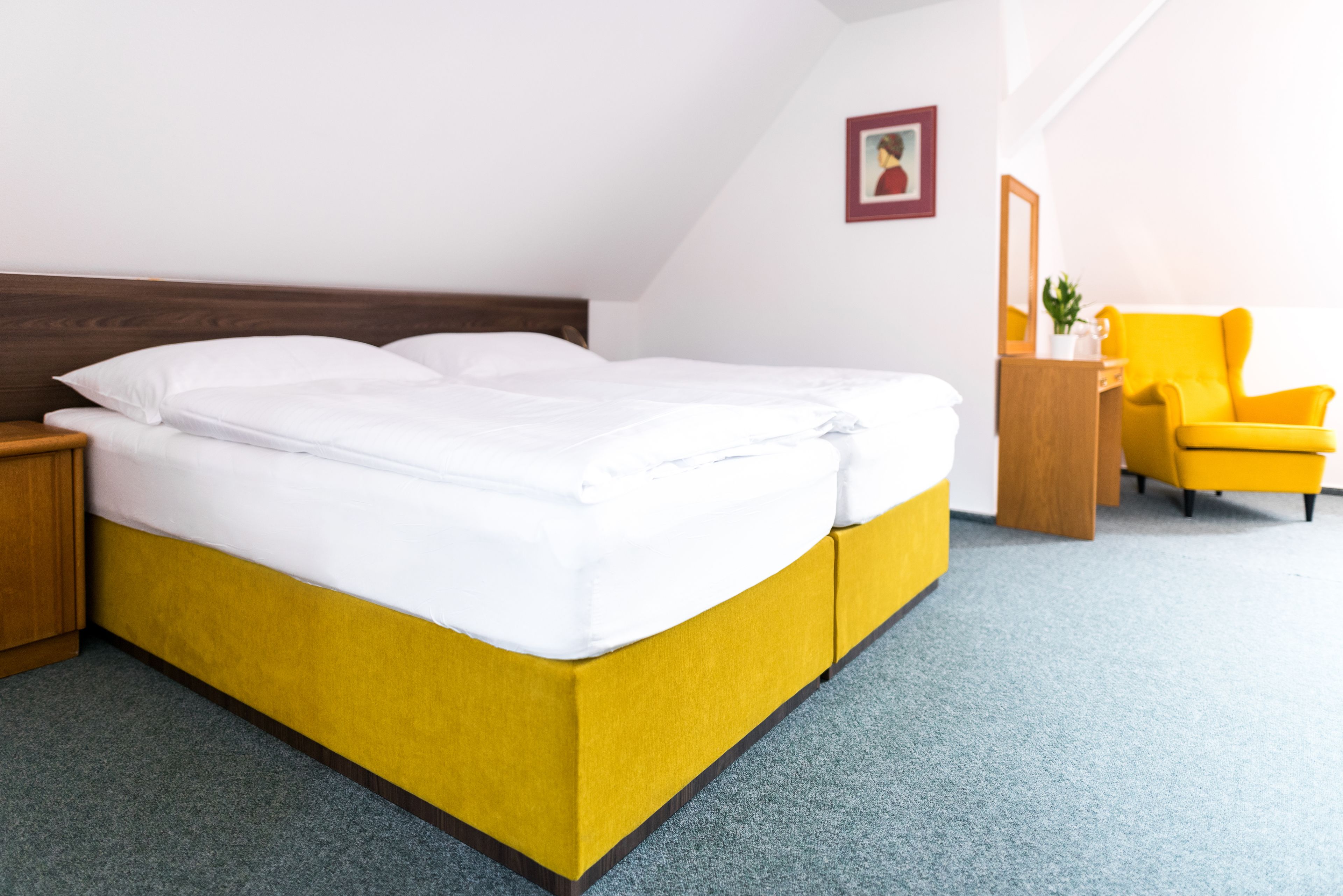 A neatly made bed with white linens in a room with a yellow accent wall and a yellow armchair.