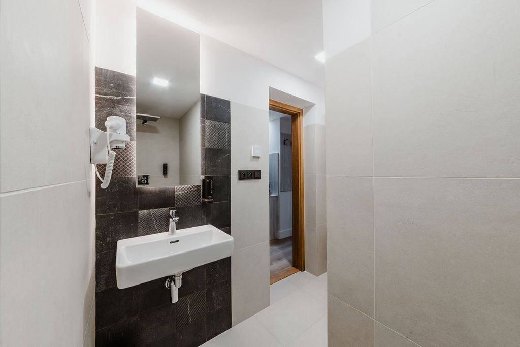 A modern bathroom with a white sink, dark patterned tiles, and a handheld hair dryer.