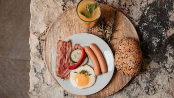 A breakfast plate with sausages, bacon, a fried egg, and a slice of bread on a wooden board.
