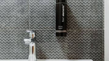 Un baño de diseño moderno, con un grifo cromado y una botella negra de jabón líquido etiquetada como "four elements".