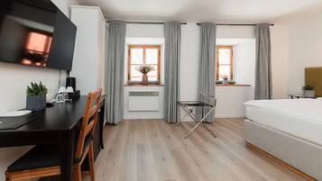 Een moderne, goed verlichte kamer met een houten eettafel, een bed en twee ramen met grijze gordijnen.