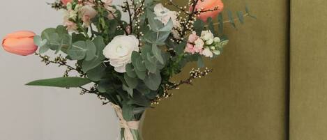 Un letto con lenzuola bianche, un tavolino di vetro con un vaso di fiori e una testiera imbottita verde.