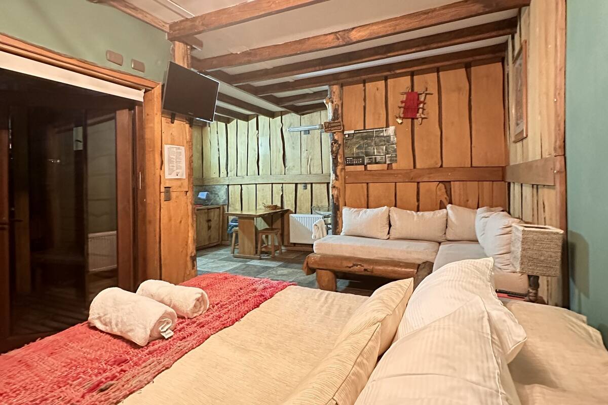 A rustic room with a wooden ceiling, a sofa, a bed with a red blanket, and a television.