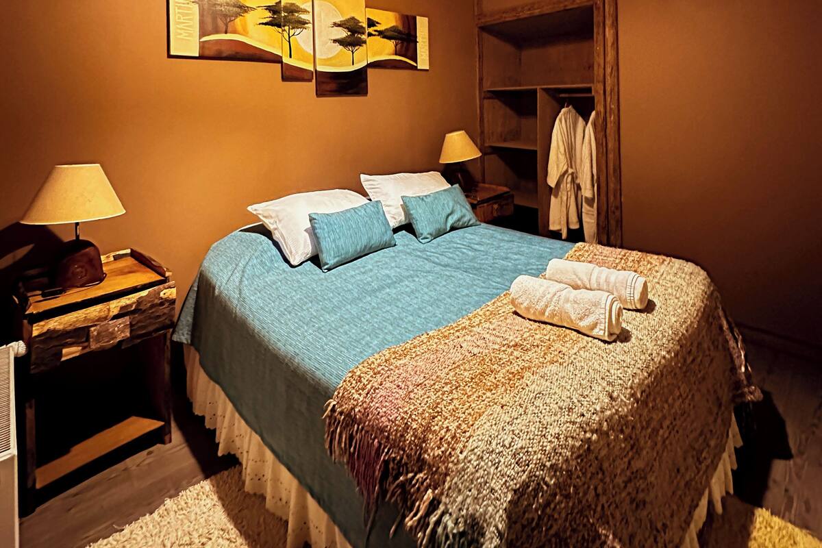 A bedroom with a bed, two bedside tables, a lamp, a wall art piece, and a wardrobe.