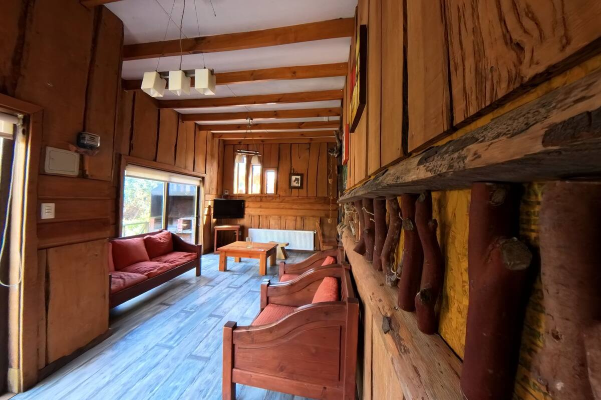 A wooden cabin interior with a sofa, wooden benches, a table, and a television.