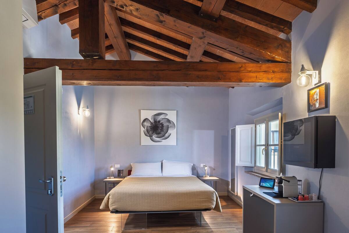 Une chambre à coucher avec un plafond en bois, un lit, une table de chevet, un bureau avec un ordinateur et une fenêtre.