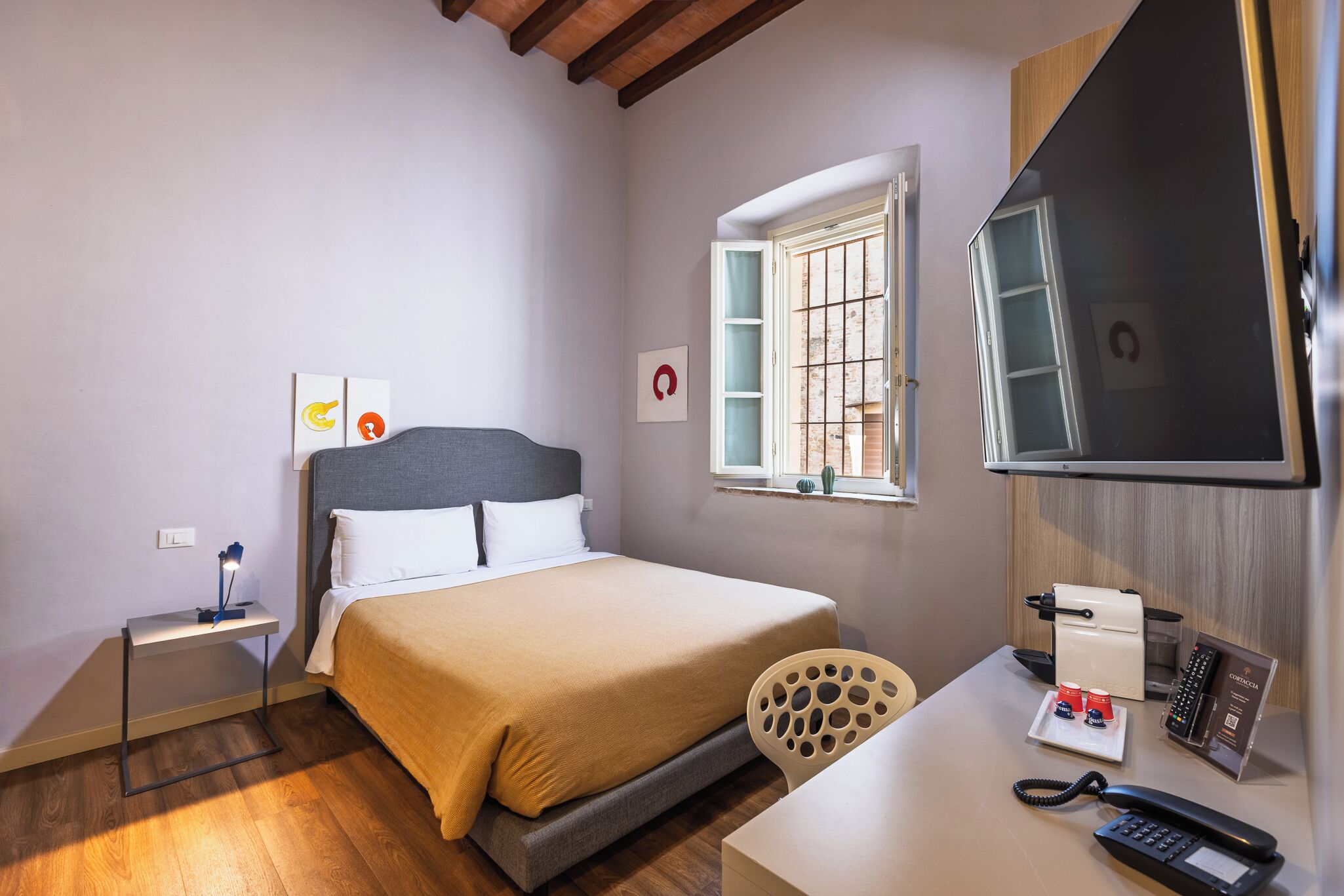 A hotel room with a bed, bedside table, chair, desk with a phone, and a TV.