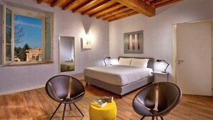 Une chambre à coucher comprenant un lit, deux chaises, une table de chevet, un miroir et une fenêtre donnant sur une maison et des arbres.
