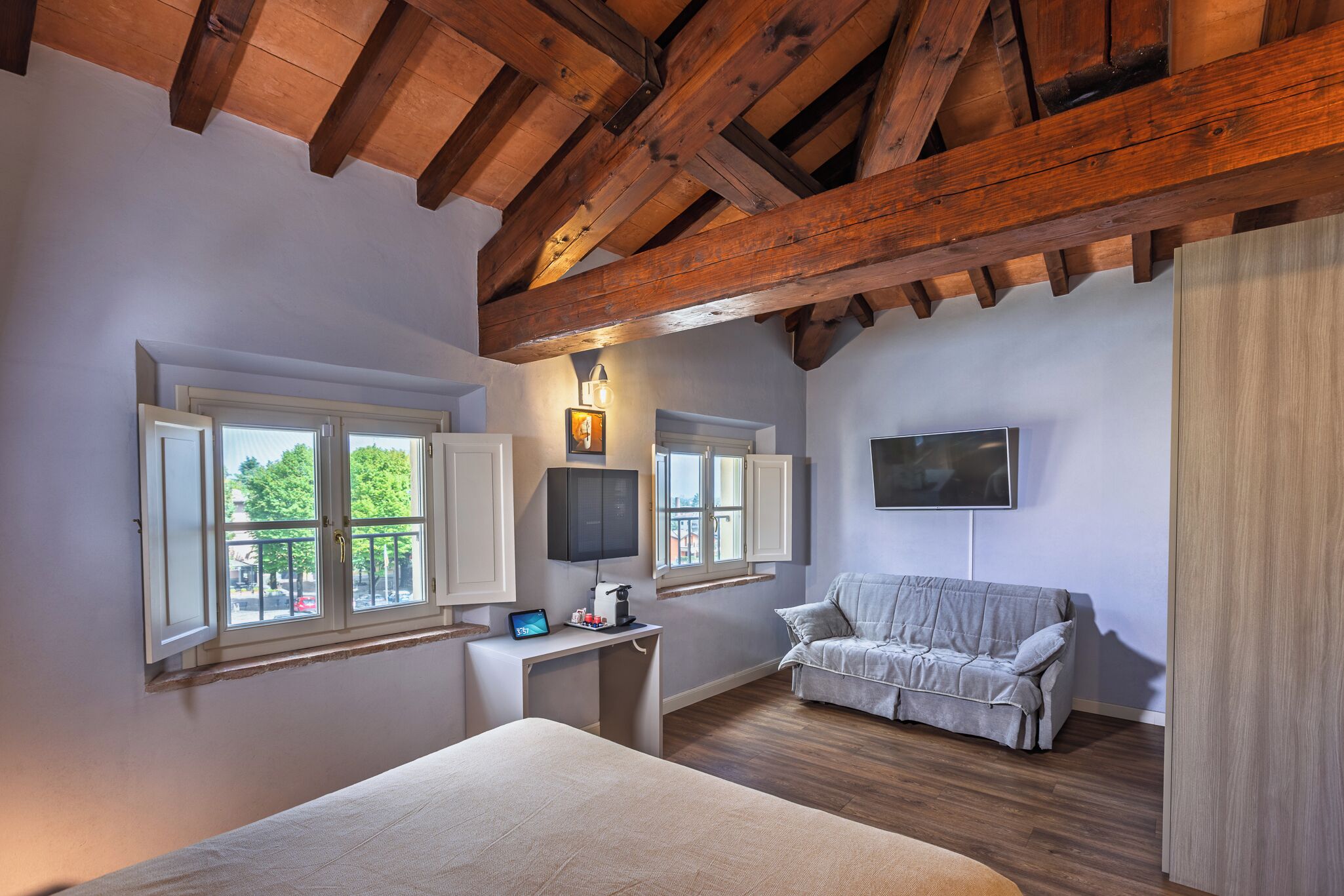 A bedroom with a wooden ceiling, a bed, a desk with a computer, a couch, and a TV.