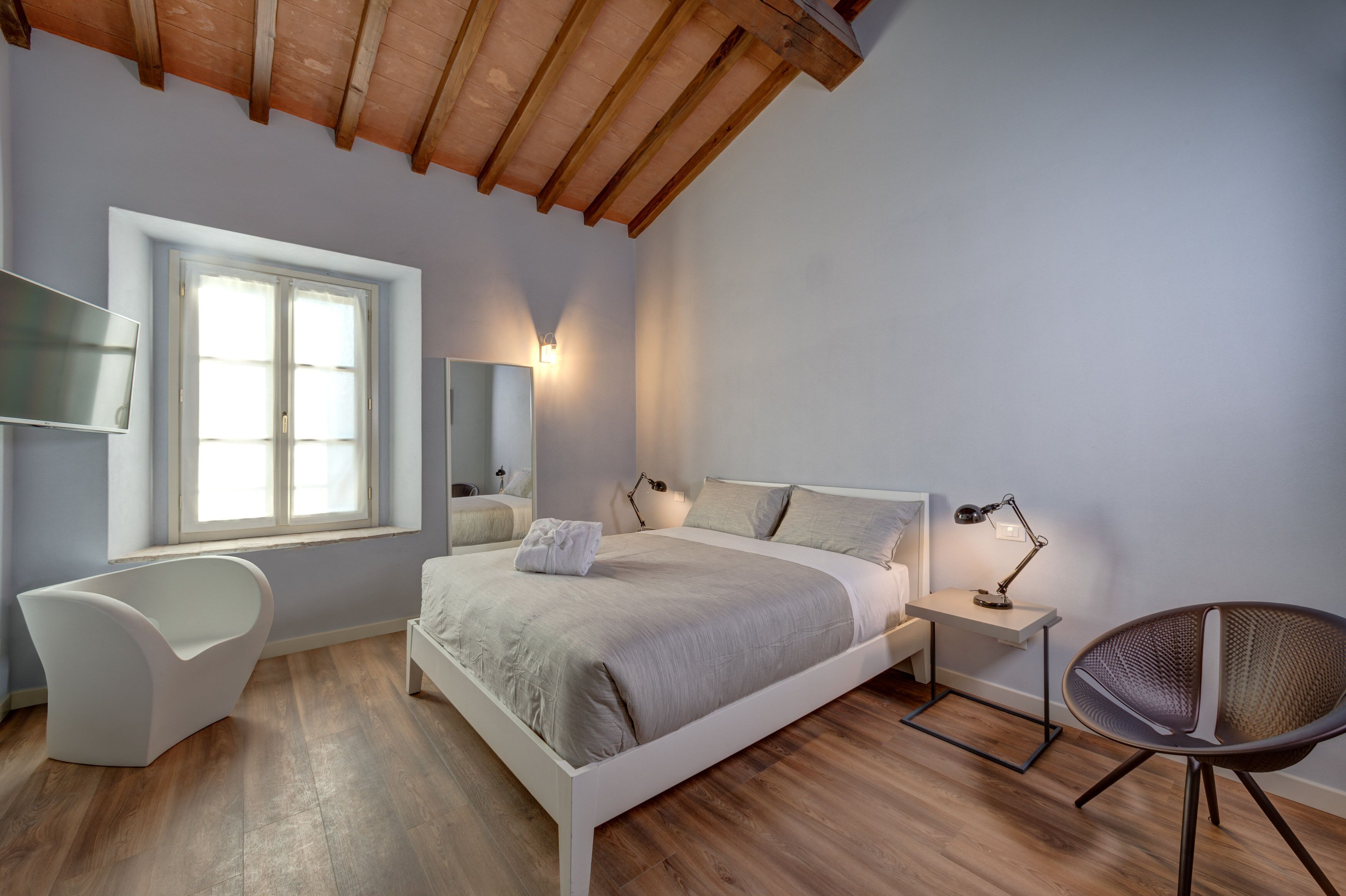 A bedroom with a bed, a chair, a desk, a lamp, and a window.