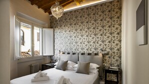 A bedroom with a large bed, a nightstand, a lamp, and a window with shutters. - Parione Uno (Florence)