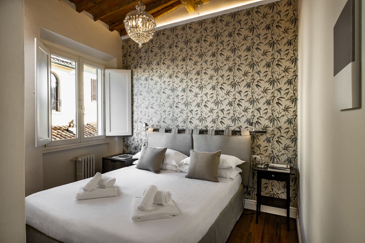 A bedroom with a large bed, a nightstand, a lamp, and a window with shutters.