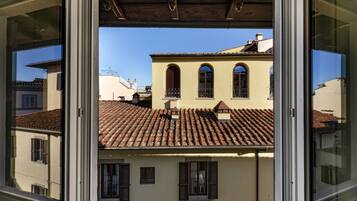 A view through a window of a building with a tiled roof, arched windows, and shutters.