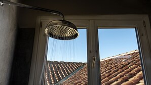 A showerhead with water flowing into a glass door, revealing a tiled roof outside. - Parione Uno (Florence)