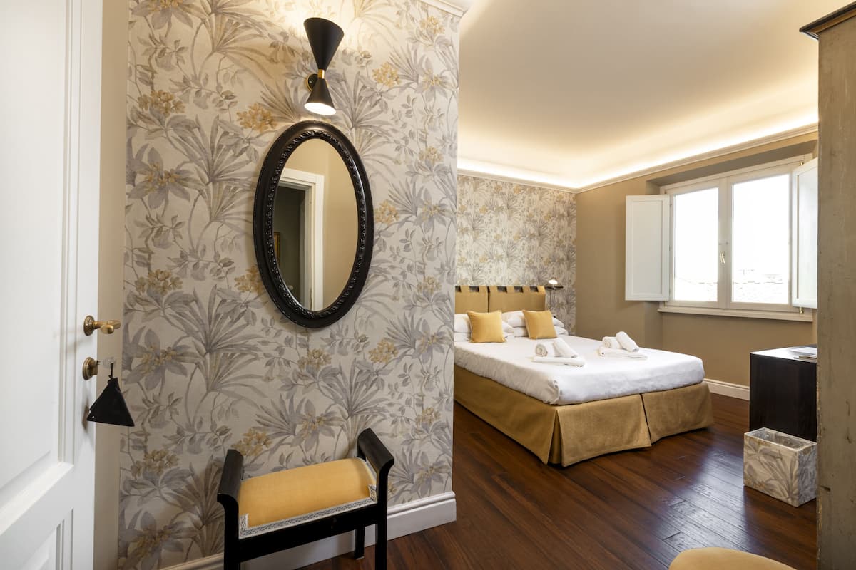 A bedroom with a bed, a bench, a mirror, and a window.