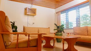Uma sala de estar com mobiliário de madeira, um ventilador de teto e uma janela com cortinas.