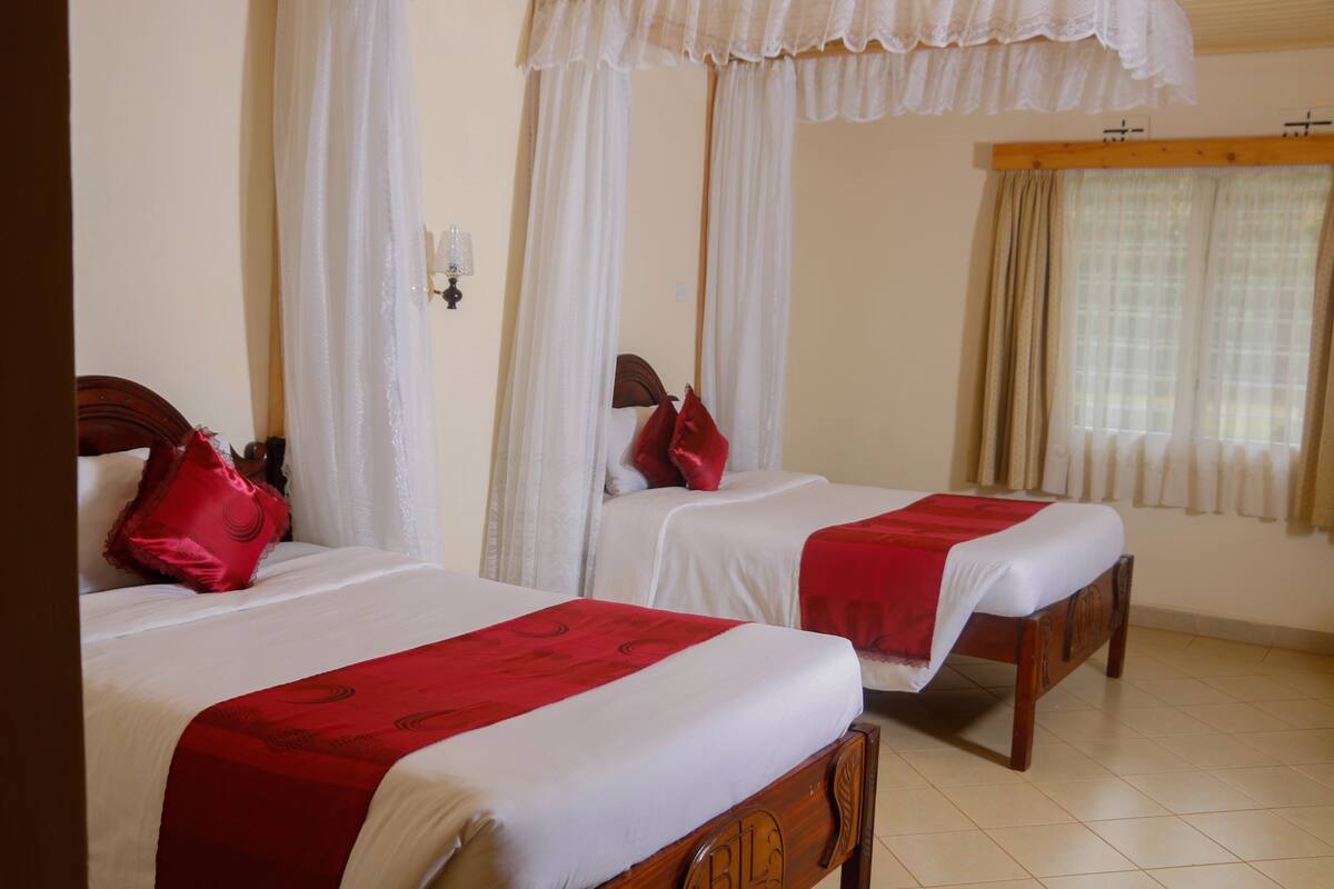 A hotel room with two single beds, each with a red blanket and pillow.