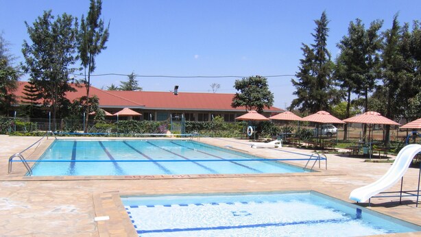 Uma piscina com área rasa, rodeada por ladrilhos de pedra, e um escorrega.