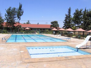 A swimming pool with a shallow end, surrounded by stone tiles, and a slide. - BTL Christian International Conference Centre (Ruiru)