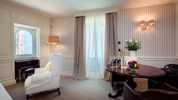 A hotel room with a white armchair, a wooden table with a vase of flowers, a bottle of champagne, and a fruit bowl.