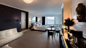 A modern hotel room with a large bed, a sitting area with a sofa and chairs, a dining table, and a Buddha statue. - Relais La Speranzina (Sirmione)