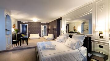 A hotel room with a large bed, a sitting area with a table and chairs, a small desk, and a bathroom with a mirror and sink.