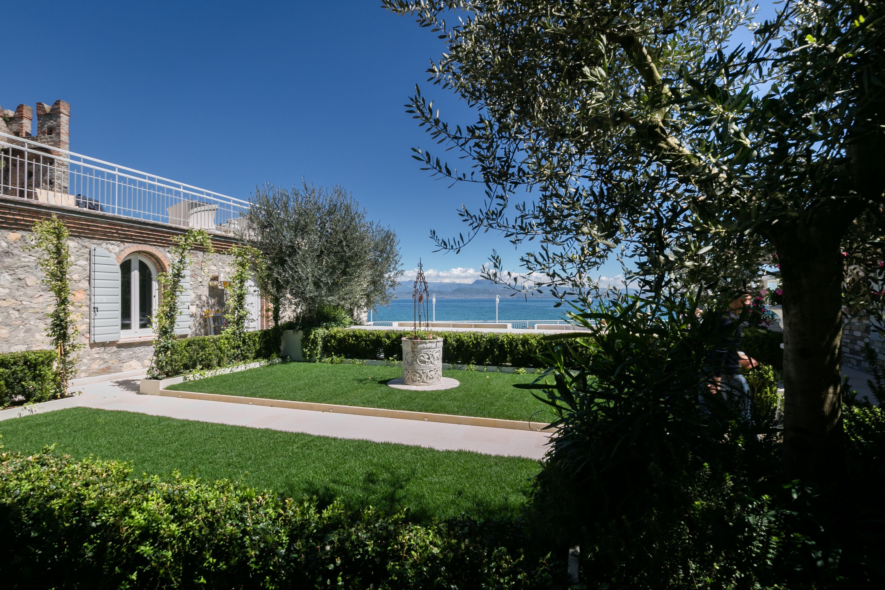 Un patio con un edificio de piedra, una fuente y vistas al mar.