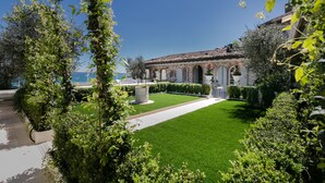 A well-maintained garden with a neatly trimmed lawn, a pathway, and a building with arches and a tiled roof. - Relais La Speranzina (Sirmione)
