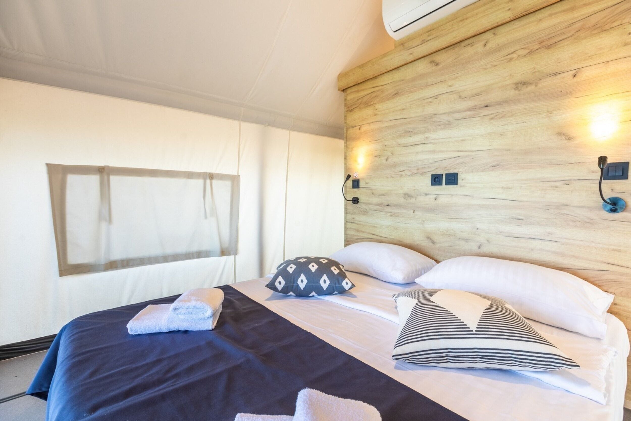 A hotel room with a bed, pillows, a blanket, and a wall-mounted light fixture.