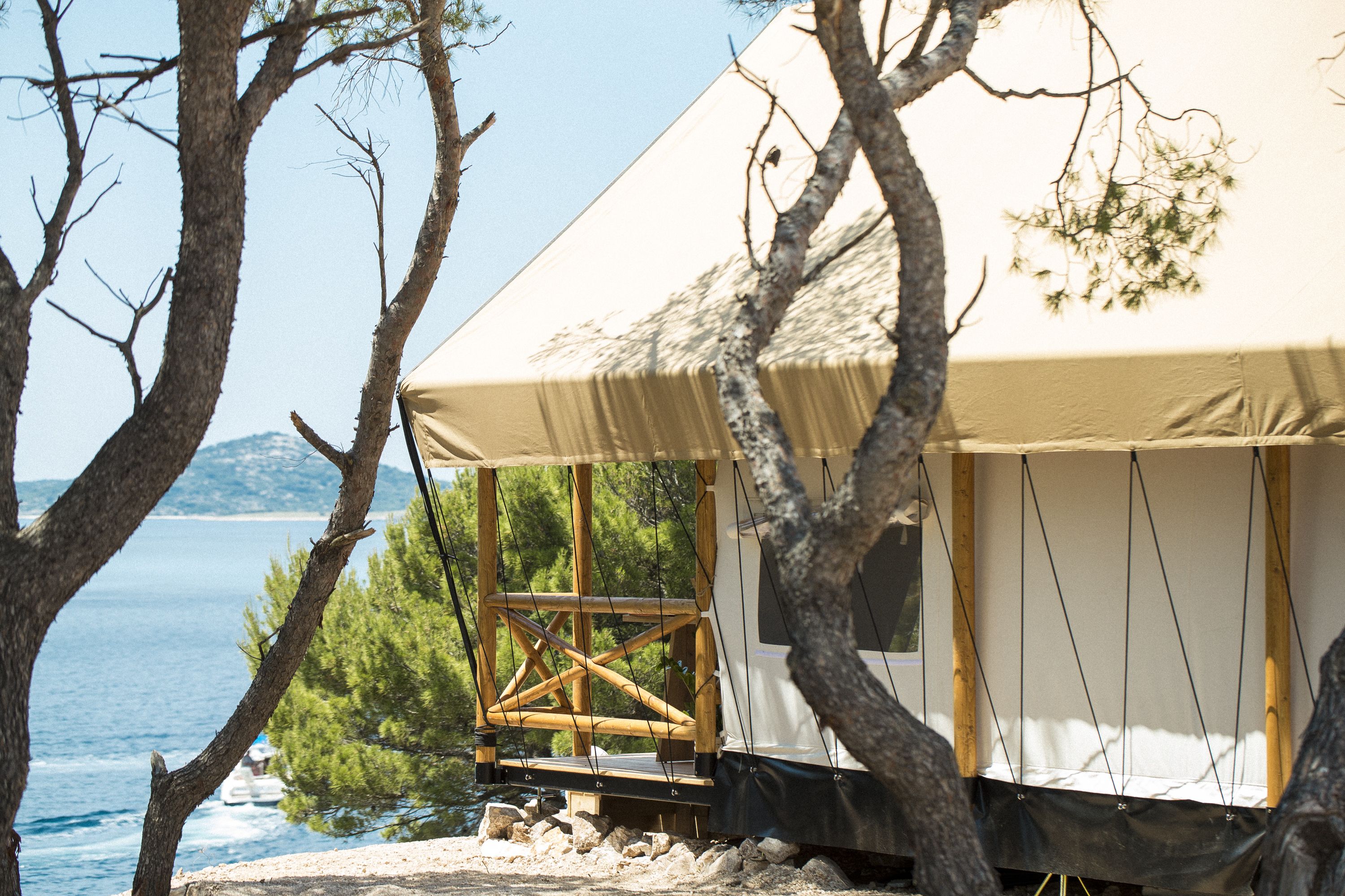 A beachside tent with a wooden deck, overlooking the sea and trees.