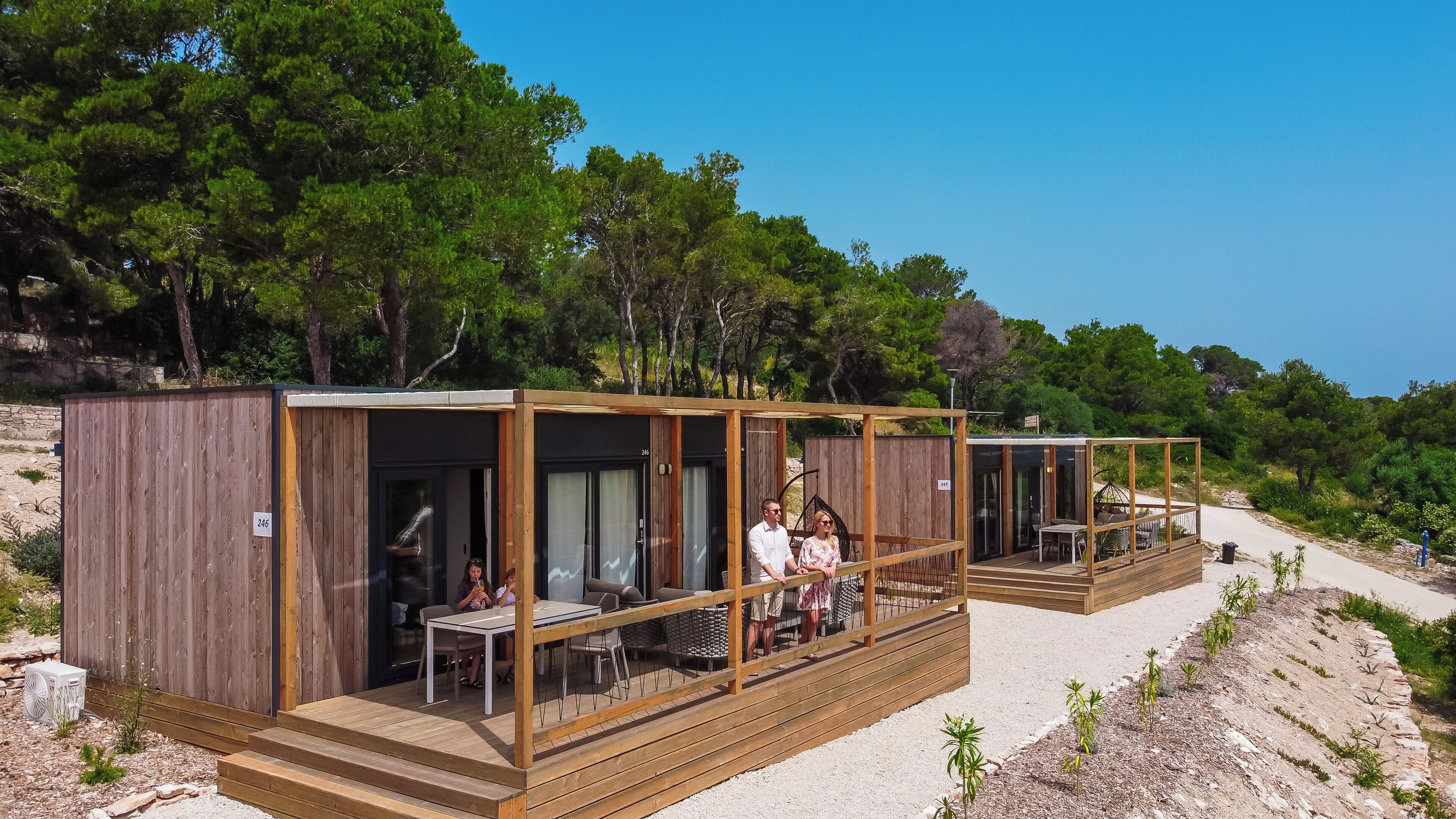 Une cabane en bois dotée d’une terrasse, d’une table et de chaises, entourée d’arbres et surplombant un ciel dégagé.