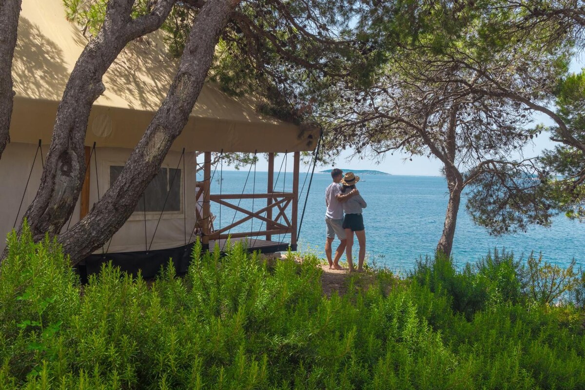 A wooden deck with a view of the sea, a covered seating area, and lush greenery.