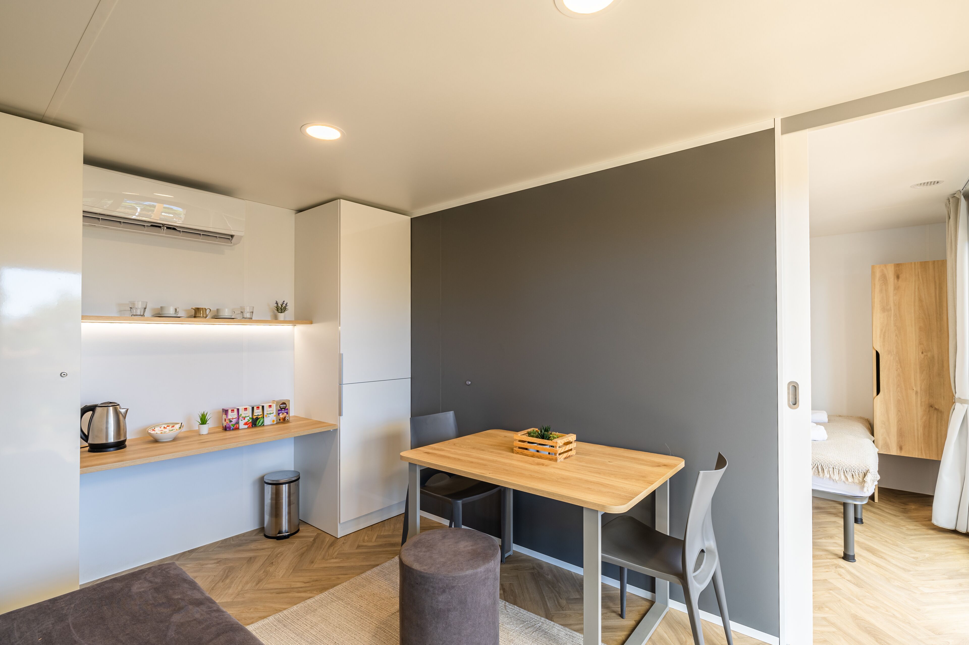 Een moderne keuken met een houten tafel, grijze stoelen en een grijze wand.
