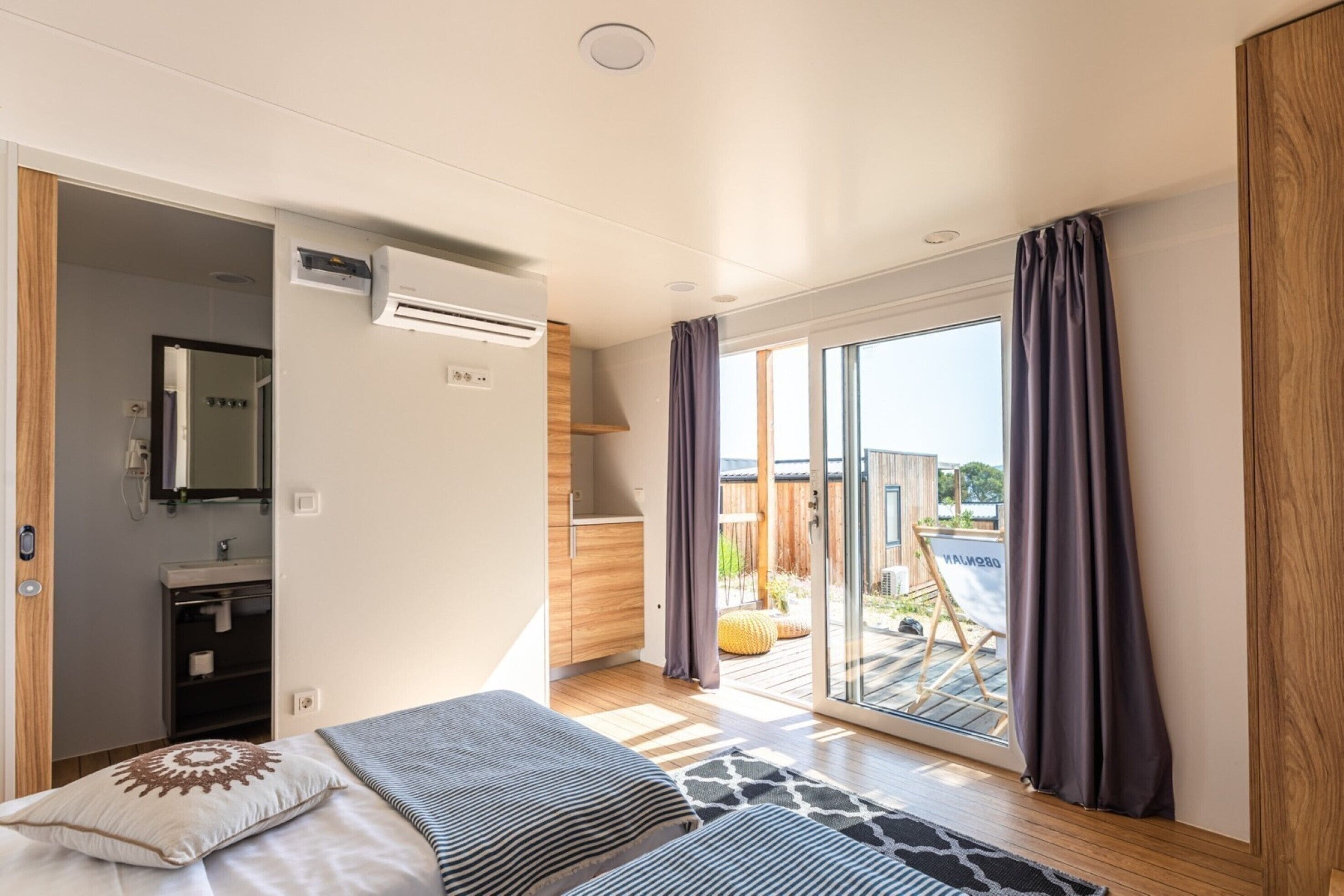A modern bedroom with a bed, a bathroom, and a sliding glass door leading to an outdoor area.