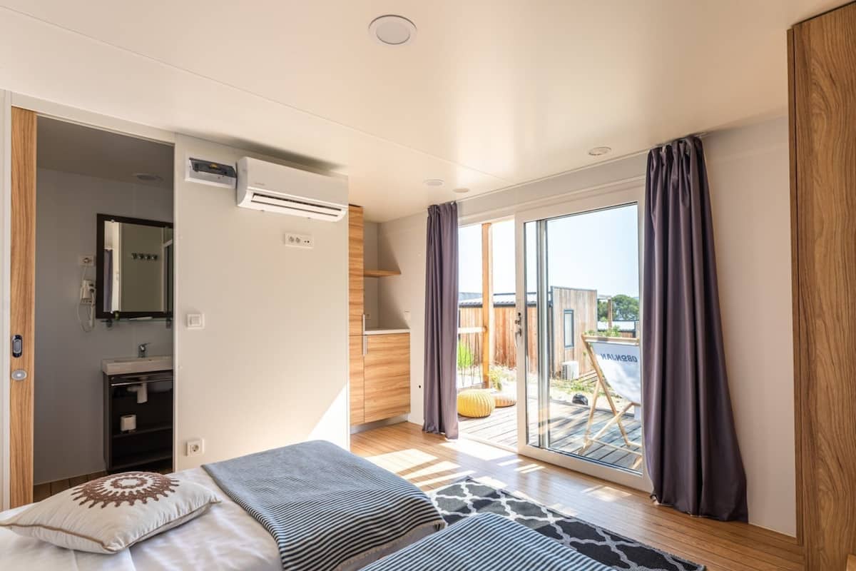 A modern bedroom with a bed, a bathroom, and a sliding glass door leading to an outdoor area.